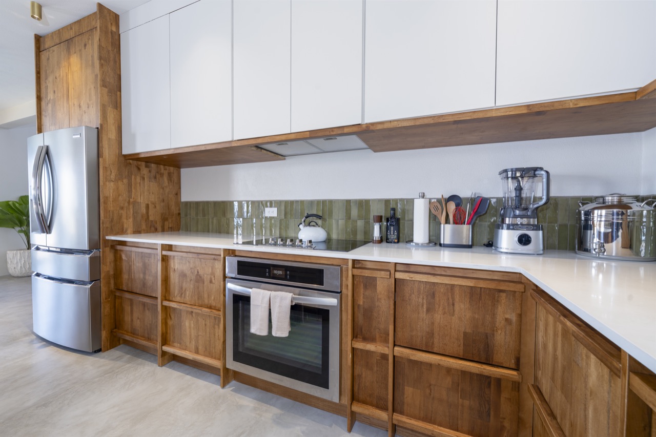 Kitchen with wood cabinetry, white upper cabinets and green tile backsplash